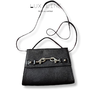 Puede incluir: Bolso bandolera de cuero negro con cierre de hebilla plateada. El bolso tiene una superficie texturizada y una correa larga y fina. El texto "LUX LINE PRETTY ILL VINTAGE" est&aacute; en la parte superior.