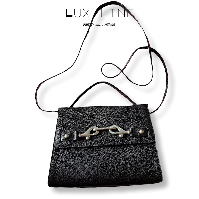 Puede incluir: Bolso bandolera de cuero negro con cierre de hebilla plateada. El bolso tiene una superficie texturizada y una correa larga y fina. El texto "LUX LINE PRETTY ILL VINTAGE" est&aacute; en la parte superior.