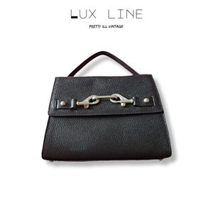 Puede incluir: Bolso de mano de cuero negro con cierre de solapa y cierre plateado. El bolso tiene un asa corta. El texto "LUX LINE" y "PRETTY ILL VINTAGE" se encuentra en la parte superior de la imagen.