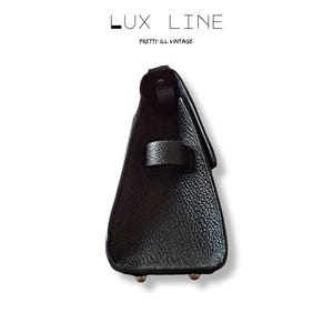 Puede incluir: Un bolso de mano de cuero negro con una superficie texturizada. El bolso tiene un cierre de solapa y un asa peque&ntilde;a. El texto "LUX LINE" y "PRETTY ILL VINTAGE" est&aacute;n impresos en la parte superior.