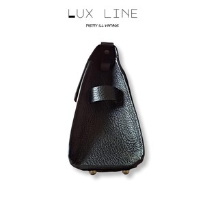 Puede incluir: Un bolso de mano de cuero negro con una superficie texturizada. El bolso tiene una correa y dos peque&ntilde;os pies met&aacute;licos. El texto "LUX LINE" y "PRETTY ILL VINTAGE" est&aacute; impreso en la parte superior.