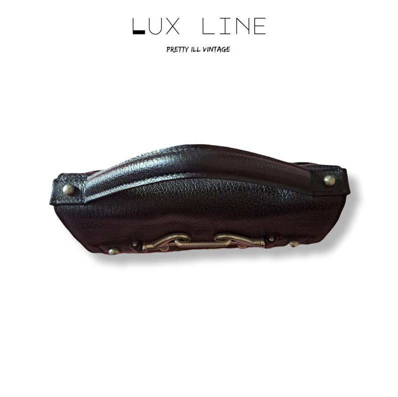 Puede incluir: Un bolso de mano de cuero negro con un asa curva y herrajes plateados. El bolso tiene una superficie texturizada y est&aacute; etiquetado "LUX LINE" y "PRETTY ILL VINTAGE" en texto blanco.