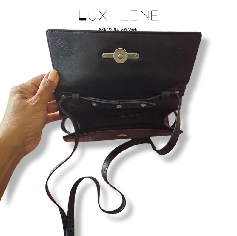 Puede incluir: Bolso bandolera de cuero negro con cierre de solapa y cierre plateado. El bolso tiene una correa larga y fina y un bolsillo interior. El texto "LUX LINE" y "PRETTY ILL VINTAGE" est&aacute;n impresos en la parte superior.