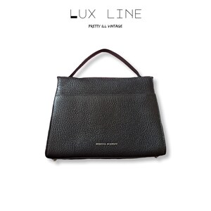 Puede incluir: Bolso de mano de cuero negro con asa superior. El bolso tiene una superficie texturizada y forma rectangular. El nombre de la marca "REBECCA MINKOFF" es visible en la parte delantera. El texto "LUX LINE" y "PRETTY ILL VINTAGE" est&aacute;n en la parte superior.