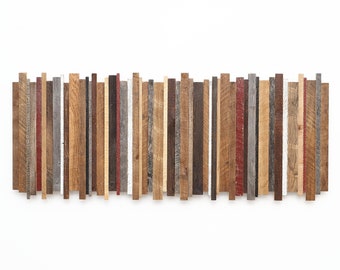 May include: A wall art piece made of various wood strips in different shades of brown, gray, and red. The strips are arranged vertically and create a textured, abstract pattern.