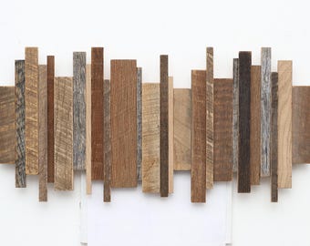 Puede incluir: Una pieza de decoración de pared hecha de varias tablas de madera de diferentes anchos y longitudes, dispuestas en una línea horizontal. Las tablas son de diferentes tonos de marrón y tienen un aspecto rústico y recuperado.