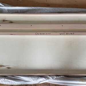 May include: The back of a wooden framed artwork with two wooden strips attached to the back for hanging. The artwork is signed "Craig Forget" and dated "Dec 2018". The wooden strips are labeled "Wall Bracket" and "1/4" Round Stick".