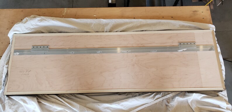 Peut inclure: L'arri&egrave;re d'un cadre rectangulaire en bois avec une bordure blanche. Une glissi&egrave;re m&eacute;tallique est fix&eacute;e au sommet du cadre &agrave; l'aide de vis. La glissi&egrave;re comporte plusieurs trous pour accrocher le cadre.