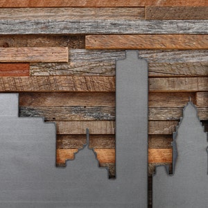 Peut inclure: Une silhouette de ville en m&eacute;tal mont&eacute;e sur un panneau de bois. La silhouette est en m&eacute;tal et peinte en argent. Le panneau de bois est en bois de r&eacute;cup&eacute;ration et pr&eacute;sente une vari&eacute;t&eacute; de couleurs et de textures.