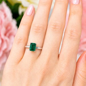 A woman's hand wearing a sterling silver ring featuring an 9x7mm emerald cut lab emerald. Model image for size and styling reference — not a photo of the actual ring.