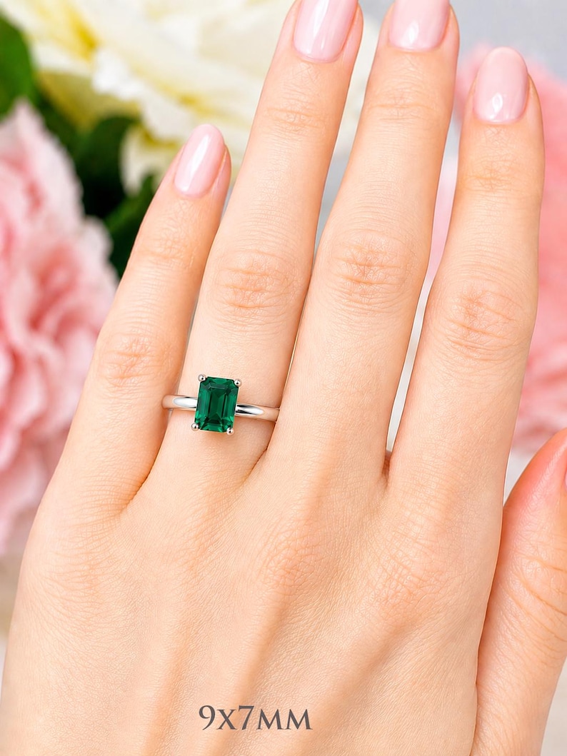 A woman's hand wearing a sterling silver ring featuring an 9x7mm emerald cut lab emerald. Model image for size and styling reference — not a photo of the actual ring.