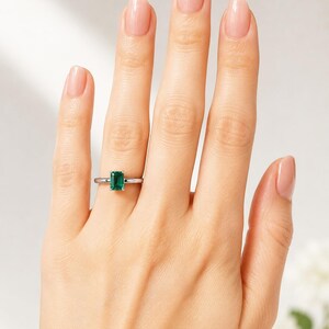 A woman's hand wearing a sterling silver ring featuring a 7x5mm emerald cut lab emerald. Model image for size and styling reference — not a photo of the actual ring.