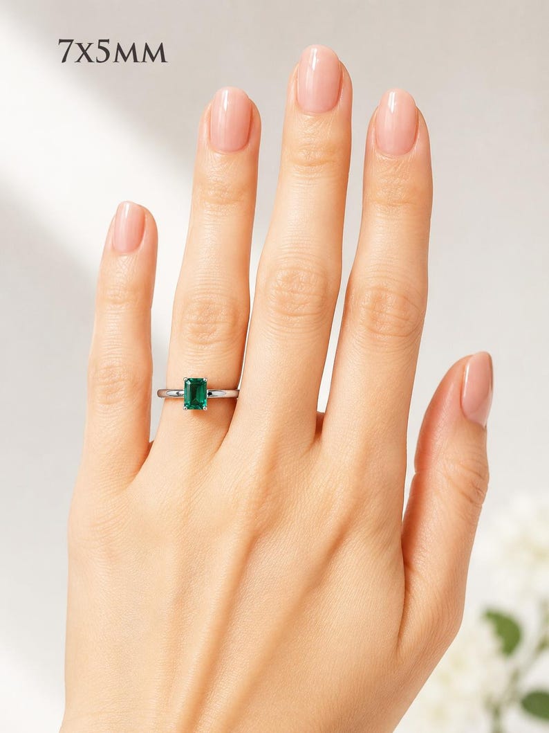 A woman's hand wearing a sterling silver ring featuring a 7x5mm emerald cut lab emerald. Model image for size and styling reference — not a photo of the actual ring.