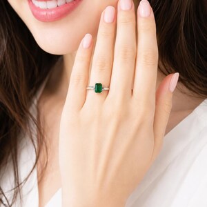 A woman wearing a sterling silver ring featuring an emerald cut lab emerald. Model image for size and styling reference — not a photo of the actual ring.