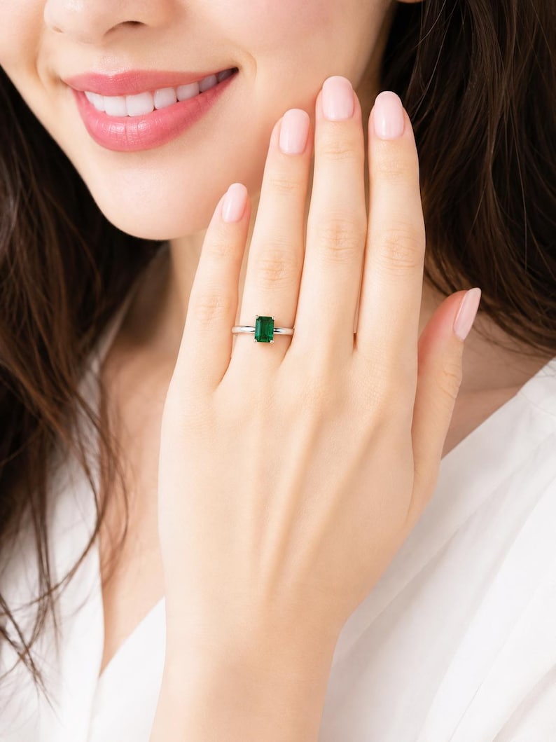 A woman wearing a sterling silver ring featuring an emerald cut lab emerald. Model image for size and styling reference — not a photo of the actual ring.