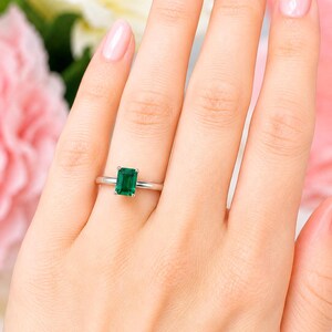 A woman's hand wearing a sterling silver ring featuring an 8x6mm emerald cut lab emerald. Model image for size and styling reference — not a photo of the actual ring.