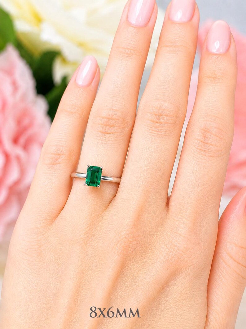 A woman's hand wearing a sterling silver ring featuring an 8x6mm emerald cut lab emerald. Model image for size and styling reference — not a photo of the actual ring.