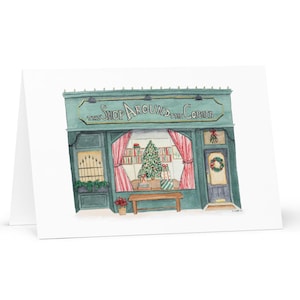 Peut inclure: Une illustration aquarelle d'une devanture de magasin verte avec le texte "The Shop Around the Corner" au-dessus de l'entrée. La vitrine du magasin est décorée de rideaux à rayures rouges et blanches, d'un sapin de Noël et de cadeaux emballés. Une couronne est accrochée à la porte.