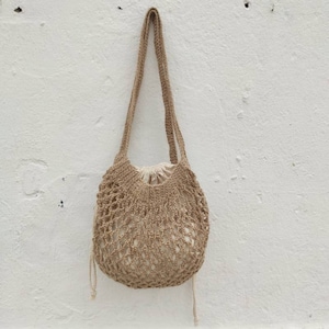 May include: A brown crocheted tote bag with a white lining. The bag has a long strap and is made of a natural fiber.