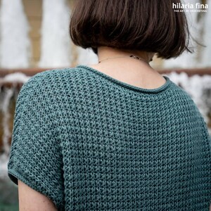 May include: A teal blue crocheted top with short sleeves. The top is made with a textured stitch pattern.