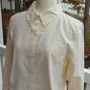 Puede incluir: Camisa abotonada de color amarillo p&aacute;lido con cuello abotonado y bolsillo en el pecho. La camisa de manga larga tiene un dise&ntilde;o cl&aacute;sico con botones en la parte delantera y en los pu&ntilde;os. La camisa se exhibe en un maniqu&iacute;.