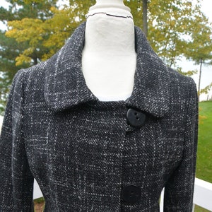 May include: A black and white tweed blazer with a collar and three black buttons. The blazer has a fitted silhouette and a slightly flared hem.
