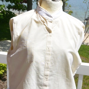 Puede incluir: Camisa crema con botones y cuello blanco. La camisa es sin mangas y tiene un corte entallado. La tela parece ser una mezcla ligera de algod&oacute;n o lino, adecuada para climas c&aacute;lidos.