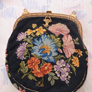Könnte beinhalten: Eine vintage schwarze Samt-Abendtasche mit goldenem Metallrahmen und Blumenstickerei. Die Stickerei zeigt eine Vielzahl von bunten Blumen, darunter blaue, rosa, gelbe und orangefarbene.