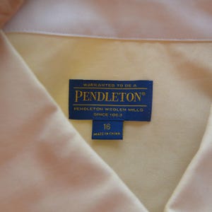 Puede incluir: Primer plano de una camisa amarillo claro con cuello blanco. Una etiqueta azul dice "WARRANTED TO BE A PENDLETON PENDLETON WOOLEN MILLS SINCE 1863". La etiqueta de talla dice "16 MADE IN CHINA".