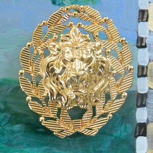 May include: A gold-colored lion's head emblem, surrounded by a laurel wreath, is the focal point of this image. The emblem is set against a backdrop of green and blue brushstrokes, with a decorative border on the right side. The lion's head is detailed and ornate.