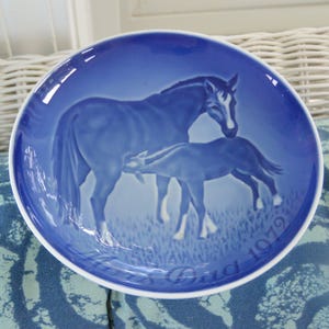 May include: A blue decorative plate featuring a horse and foal in a field. The plate has a white rim and the words "Mother's Day 1979" are inscribed on the bottom. The horses are a lighter shade of blue.