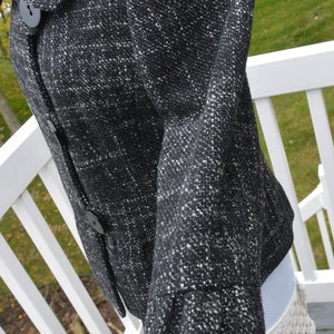 May include: A black and white tweed jacket with a button closure. The jacket has a collar and long sleeves.