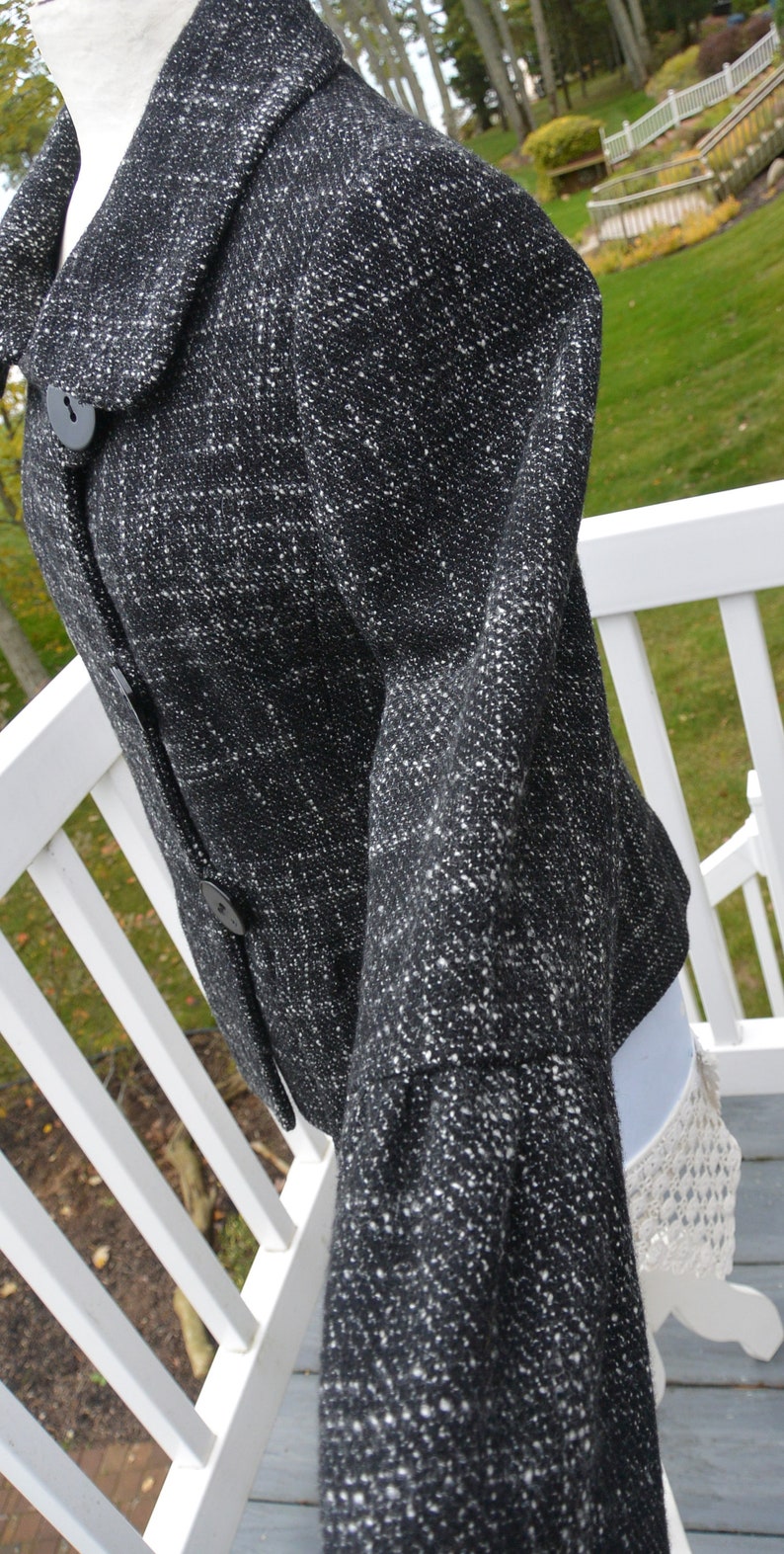 May include: A black and white tweed jacket with a button closure. The jacket has a collar and long sleeves.