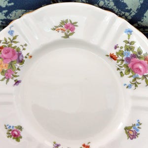 May include: A white porcelain saucer with a gold rim and a floral design featuring pink, purple, and yellow flowers.