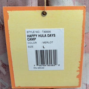 May include: A yellow tag with an orange border is suspended by a string. The tag displays the text "HAPPY HULA DAYS CAMP" and "MERLOT" color. The size is listed as "L". A barcode and the number "7 49784 95582 2" are also visible.