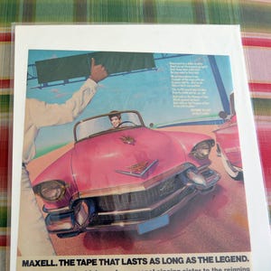 May include: Vintage advertisement featuring a pink Cadillac convertible with a person behind the wheel. A person in a white shirt gives a thumbs up. The text "MAXELL. THE TAPE THAT LASTS AS LONG AS THE LEGEND" is at the bottom.