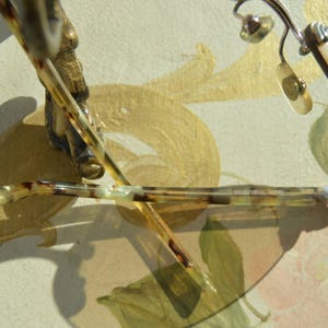 May include: Close-up of eyeglasses with a tortoiseshell pattern on the arms and a silver frame. The lenses are clear, and the glasses are resting on a surface with a floral design.