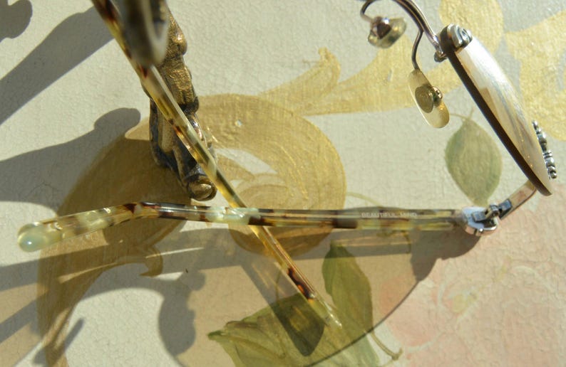 May include: Close-up of eyeglasses with a tortoiseshell pattern on the arms and a silver frame. The lenses are clear, and the glasses are resting on a surface with a floral design.