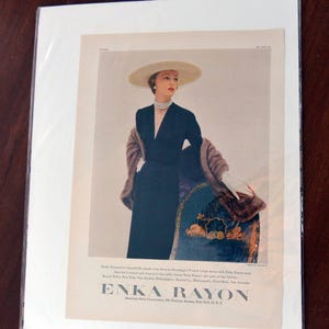 May include: Vintage fashion advertisement featuring a woman in a black dress, a wide-brimmed hat, and a fur stole. The ad includes the text "ENKA RAYON" and mentions the American Enka Corporation.
