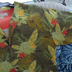 K&ouml;nnte beinhalten: Olivgr&uuml;nes Button-Down-Hemd mit tropischem Blumenmuster. Das Hemd hat gro&szlig;e gr&uuml;ne und gelbe Blumen, rote Akzente und Palmfarn. Das Hemd ist aus leichtem Stoff gefertigt und hat ein rotes Futter.