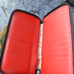 May include: Open black leather wallet with a vibrant red interior. The wallet features multiple card slots, a zippered pocket, and a larger compartment. The brand name "Tidola" is embossed on the interior. The wallet is open, revealing its organizational design.