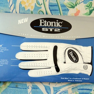 May include: White golf glove with black accents and a white Etonic logo. The packaging features the text "New Air Technology Golf Gloves" and "The Lightest, Most Comfortable Fit in Golf."