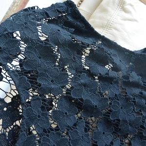 Op de afbeelding: Zwarte kanten top met een bloemenpatroon. De top is gemaakt van een delicate, open geweven stof. Het label luidt "Talbots". De top hangt aan een doorzichtige hanger.