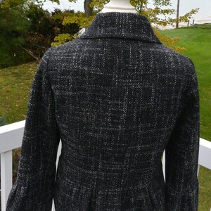 May include: Black and white tweed jacket with a fitted silhouette and a ruffled hem. The jacket has a collar and long sleeves.