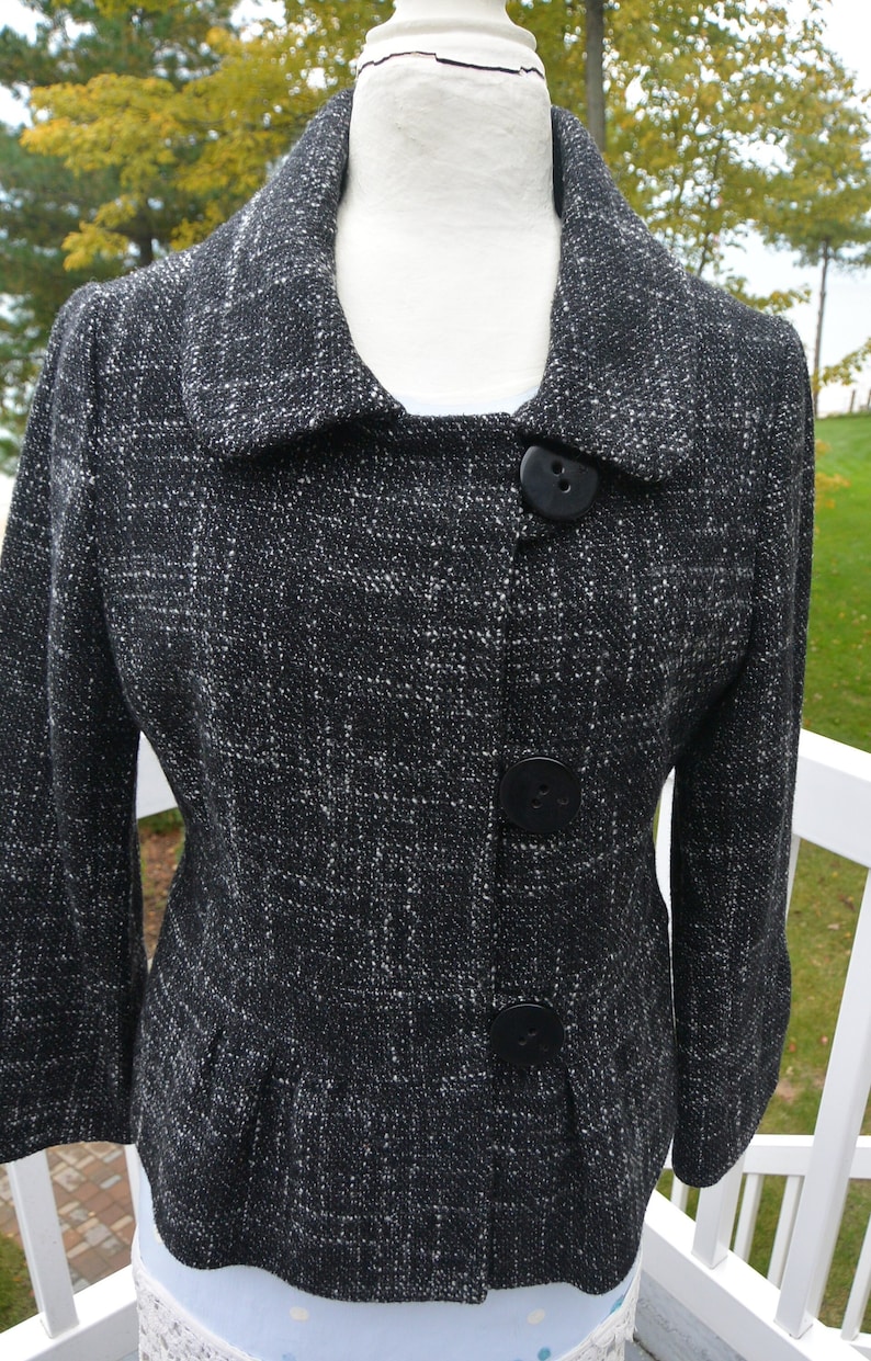 May include: A black and white tweed blazer with a collar and three black buttons. The blazer has a fitted silhouette and a slightly flared hem.