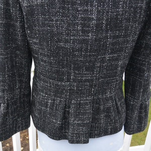 May include: Black and white tweed jacket with a ruffled hem and bell sleeves.