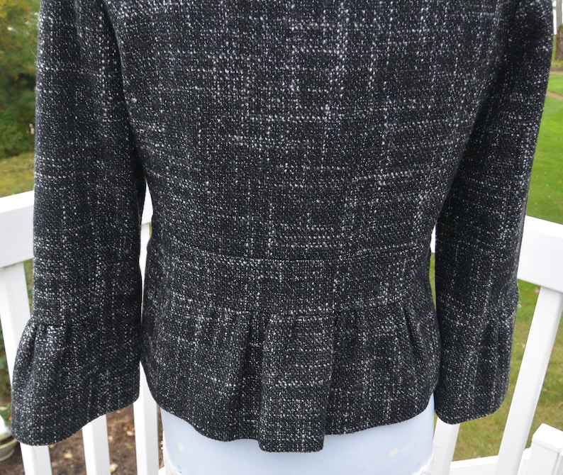 May include: Black and white tweed jacket with a ruffled hem and bell sleeves.