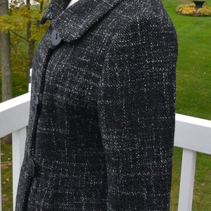 May include: A black and white tweed jacket with a button closure and a collar. The jacket has a slightly flared hem and is made of a soft, textured fabric.