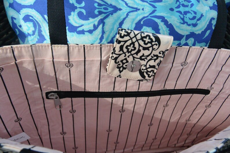 May include: A tote bag with a pink interior featuring black vertical stripes and small heart-shaped designs. A small, patterned wallet with a silver clasp is attached. The background includes a blue patterned fabric.
