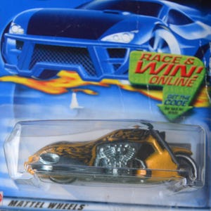 May include: A toy motorcycle in a clear plastic package. The motorcycle is yellow and black with flame details. The packaging has the text "RACE & WIN! ONLINE" and "SCORCHIN' SCOOTER".
